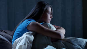 一位年輕女性夜晚獨自坐在床上，若有所思。