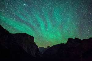 夜間黑暗山峰上方的綠色極光和星星