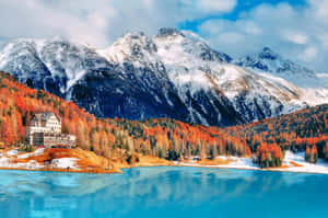 一座宏偉的酒店在湖邊，背景有秋樹和雪山。 — 風景動圖 壁紙
