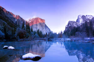 黎明時分白雪覆蓋的優勝美地山谷，山脈與河流在平靜的水面上倒映。