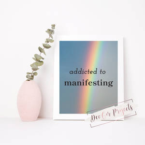 裱框印刷品，帶有彩虹和文字「addicted to manifesting」，旁邊是一個粉紅色花瓶，插著尤加利葉。
