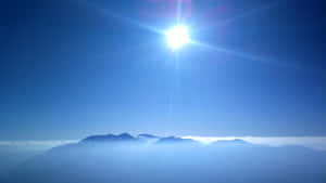 太陽穿過大氣薄霧，在山峰上明亮地照耀。 — 藍天 壁紙