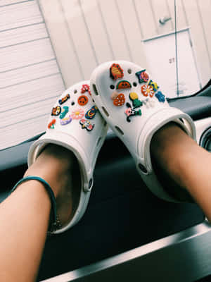 穿著白色Crocs鞋的腳，鞋上帶有彩色飾物，擱在汽車儀表板上。