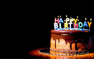 朱古力生日蛋糕，上面有點燃蠟燭在木桌上拼出 happy birthday。