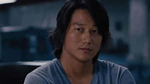 一個深色頭髮的男人在昏暗的藍色房間裡直視鏡頭。 — 狂野時速 壁紙