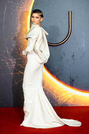 Zendaya 身穿白色長裙，站在紅地毯上，身後有宇宙燈光。