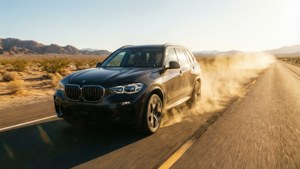 黑色BMW SUV在沙漠公路高速行駛，夕陽下揚起塵土。