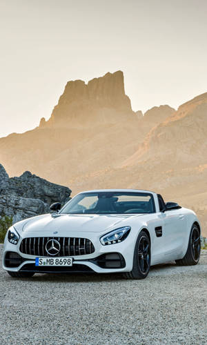 白色 Mercedes-AMG GT Roadster 停泊在碎石上，靠近岩石山脈，日落時分。