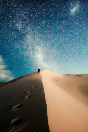 一個人在星空夜空下走上沙丘，銀河可見。