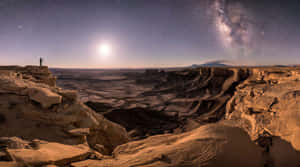 夜晚在銀河與明月下，站在沙漠懸崖上的人。 — 星星 壁紙