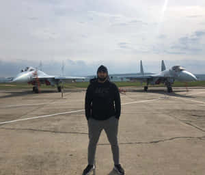 穿著UFC連帽衫的男子站在機場上兩架戰鬥機前。