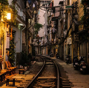 夜晚城市小巷，有鐵路軌道和暖燈下停泊的電單車。