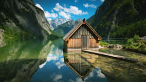 木屋漂浮在清澈的山湖上，完美倒映，背景是白雪覆蓋的山峰。 — 自然 壁紙