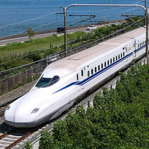 一列高速子彈列車沿著海岸鐵路行駛，附近有海洋和綠地。