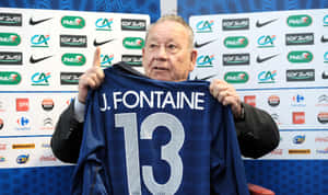 男子舉起一件印有 J Fontaine 和 13 號的藍色足球球衣。 — 足球 壁紙