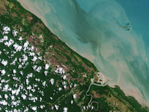 沿海景觀的衛星視圖，包含森林、雲朵和碧綠海水。 — 藝術 壁紙