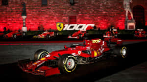 紅色法拉利F1賽車在夜間展示，前面是發光的磚牆，上面有「100」和躍馬標誌。