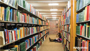 一名學生在圖書館高書架之間的地板上閱讀。
