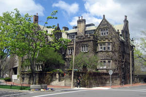 歷史石建築，爬滿常春藤，前面有樹木和街道。