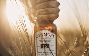 手在金色麥田中拿著Bowmore 15年威士忌瓶。