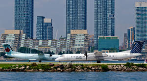 兩架波特航空的渦輪螺旋槳飛機停在城市跑道旁，旁邊有水。