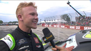 NASCAR車手在賽道上接受採訪，背景有觀眾。