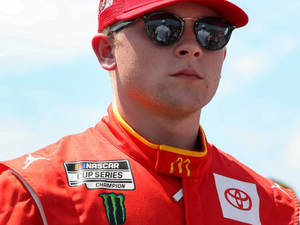 身穿紅色賽車裝備、戴著太陽眼鏡的NASCAR冠軍，戶外。
