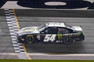 黑色 NASCAR 賽車在夜間越過終點線，帶有格仔旗。