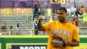 身穿黃色LSU Tigers球衣的棒球選手在體育館拿著球和手套。