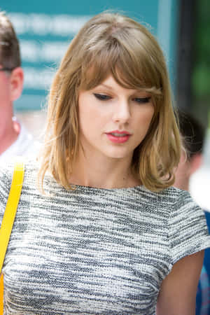 Taylor Swift 身穿灰色質感上衣，搭配黃色肩帶手袋，在戶外。