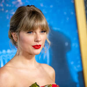 Taylor Swift 身穿紅色連衣裙，塗著大膽的紅色唇膏，在藍色活動背景下。