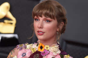 Taylor Swift 在格林美獎頒獎禮上身穿花卉裙，背景有金色獎盃。