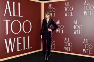 Taylor Swift 身穿紫色天鵝絨西裝，在一個有「ALL TOO WELL」文字牆的活動中擺姿勢。