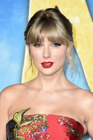 Taylor Swift 在活動中穿著紅色花卉禮服，塗著紅色唇膏。