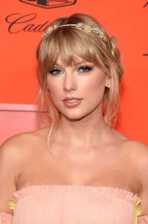 Taylor Swift 在活動中穿著粉紅色連衣裙和金色頭帶。