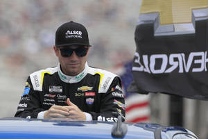 NASCAR車手穿著賽車裝備坐在賽道上的藍色賽車上。