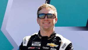 NASCAR車手身穿賽車服微笑，太陽眼鏡反射體育場。
