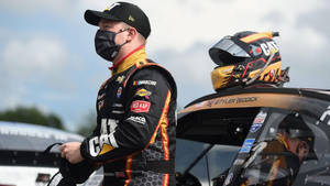 NASCAR車手Tyler Reddick身穿賽車服，頭盔放在車頂上，站在他的賽車旁。