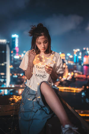 女性夜晚在城市屋頂上手持發光的仙女燈。