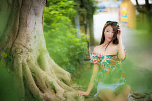 一位穿著花卉上衣的女子坐在陽光普照的公園裡一棵大樹旁。