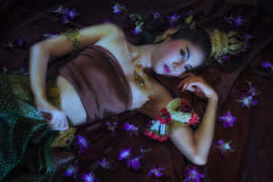 一位身穿傳統金色和棕色服飾的女性，在紫色蘭花床上休息。
