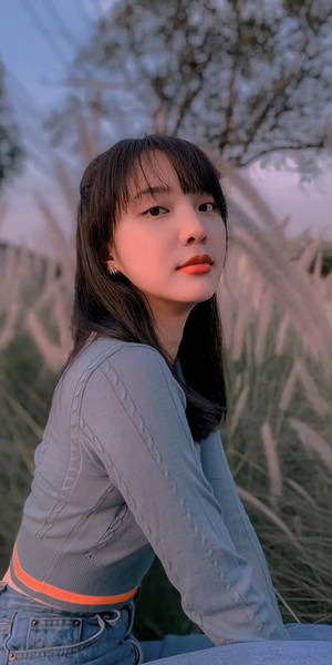 身穿牛仔褲和灰色上衣的年輕女性，在黃昏時分坐在戶外，沐浴在柔和的光線中。