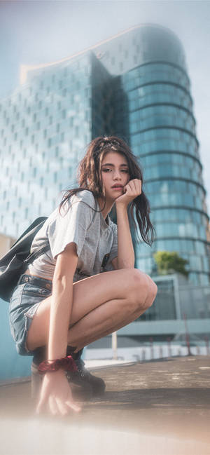 年輕女性在現代玻璃建築前若有所思地蹲著。