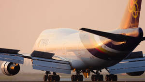 泰國航空珍寶客機在夕陽下滑行，金色光線反射在機身上