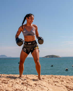 身穿UFC裝備的女性MMA拳手在陽光海灘上微笑，背景有海洋和島嶼。