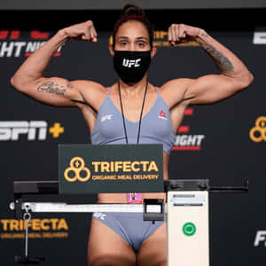 女UFC拳手在稱重時彎曲手臂，戴著口罩和灰色裝備。