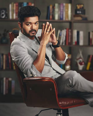 穿著灰色西裝的男人坐在紅色皮椅上，身後有書架。