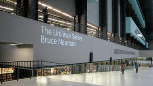 人們走過一個現代藝術博物館，有一個大型標誌寫著「The Unilever Series: Bruce Nauman」。 — 藝術 壁紙