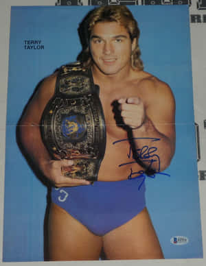 摔角手 Terry Taylor 身穿藍色短褲，手持帶有簽名的冠軍腰帶。