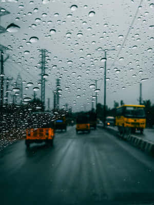 車窗上的雨滴俯瞰著濕漉漉的城市街道，有黃色巴士和卡車。